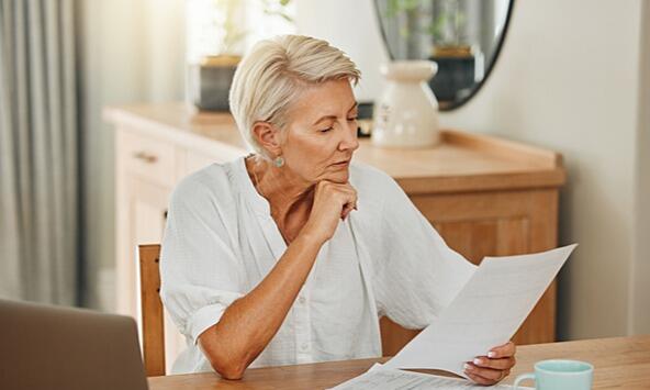 woman sitting at table looking through documents with laptop and mug nearby